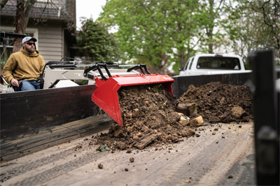 KM500 Loader - The Ventrac Loader dumping excess dirt into the back of a trailer from the side.