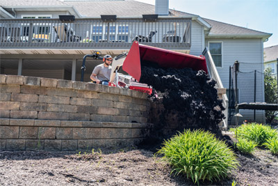 Light Material Bucket - The Ventrac Light Material Bucket dumping a large pile of mulch over a retaining wall to avoid damaging landscaping.