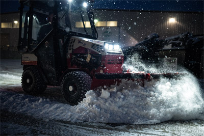 Ventrac V-Blade - Before the sun rises, the Ventrac 4520 with a V-Blade pushes through deep snow, its bright work lights illuminating the job site. The operator stays warm inside the enclosed cab, clearing large accumulations with precision. Even in the early hours, the compact tractor ensures the job gets done efficiently.