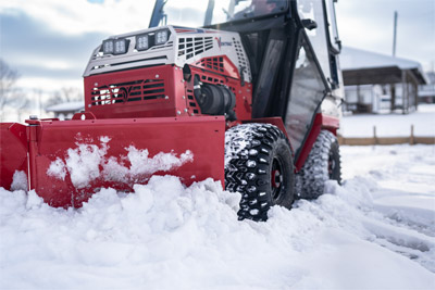 Ventrac V-Blade - A Ventrac 4520 with a V-Blade attachment clears a small parking lot, pushing heavy snow into neat piles. The blade’s angled position directs the snow efficiently, revealing clean pavement underneath. The tractor’s compact design allows it to maneuver easily in tight spaces.