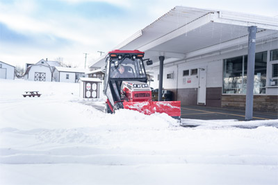 Ventrac V-Blade - The Ventrac 4520, equipped with a V-Blade, clears snow from beneath a building overhang. Its low-profile design allows the operator to work close to structures, removing snow where larger equipment would struggle to fit.